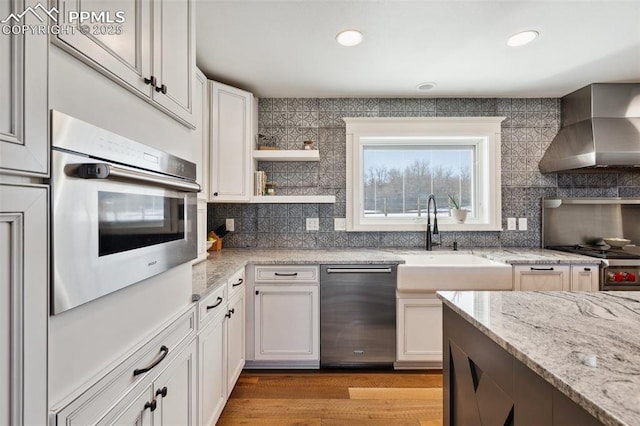 kitchen featuring light stone counters, stainless steel appliances, a sink, wall chimney range hood, and decorative backsplash