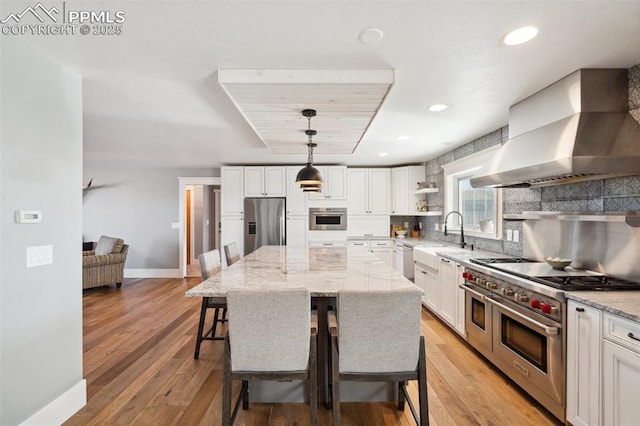 kitchen featuring wall chimney exhaust hood, appliances with stainless steel finishes, a breakfast bar, open shelves, and a sink