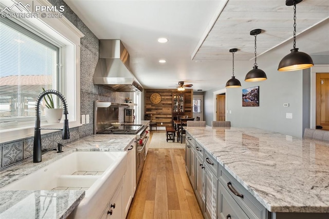 kitchen featuring wall chimney exhaust hood, light wood-style flooring, a fireplace, open shelves, and a sink