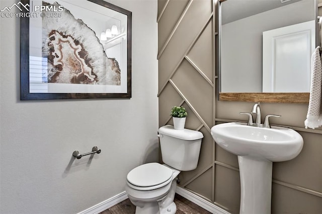 half bathroom with toilet, wood finished floors, and baseboards