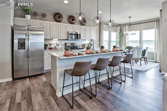 kitchen with a center island with sink, dark wood-style flooring, light countertops, appliances with stainless steel finishes, and a kitchen bar