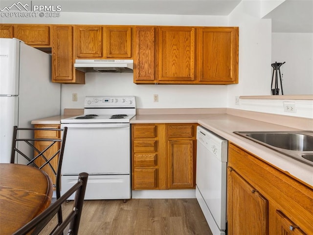 kitchen with brown cabinetry, white appliances, light countertops, and under cabinet range hood