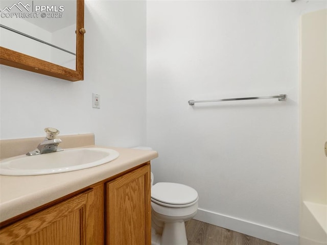 full bath featuring baseboards, toilet, a bathing tub, wood finished floors, and vanity