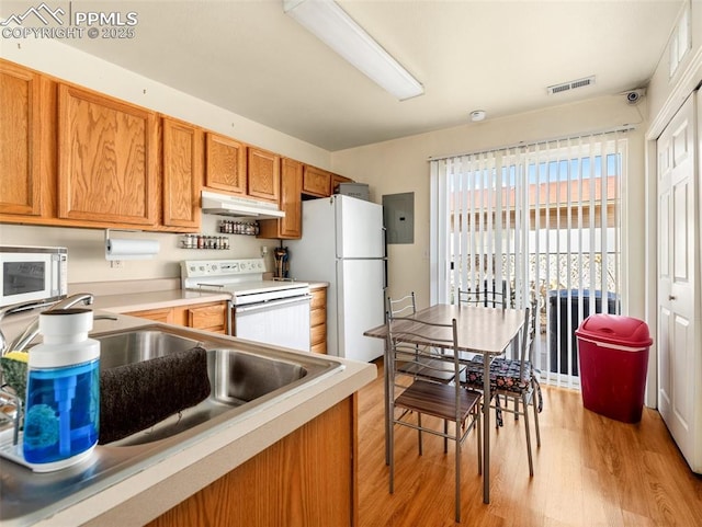 kitchen with under cabinet range hood, white appliances, visible vents, brown cabinets, and light wood finished floors