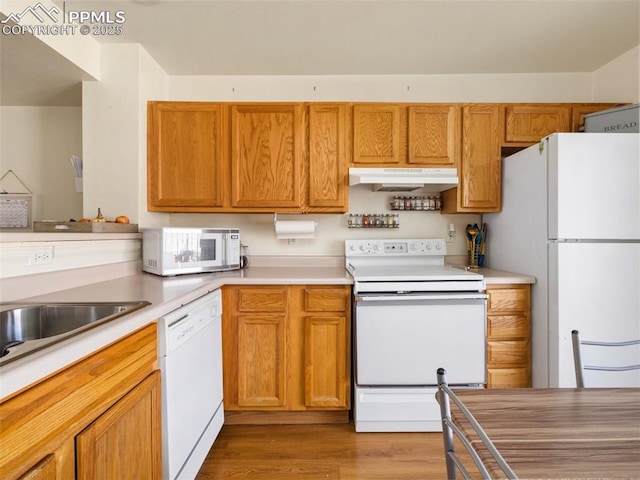 kitchen with white appliances, under cabinet range hood, light countertops, and wood finished floors