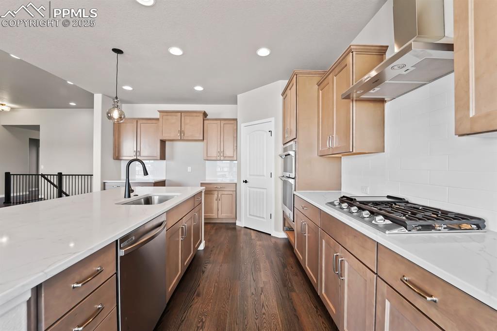 kitchen featuring dark wood-style flooring, hanging light fixtures, appliances with stainless steel finishes, a sink, and wall chimney exhaust hood