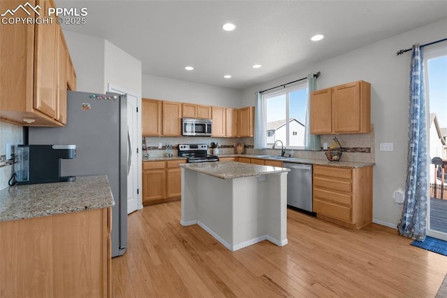 kitchen with stainless steel appliances, a kitchen island, a sink, light stone countertops, and light wood finished floors