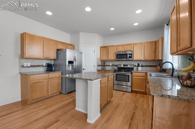 kitchen with light wood-style floors, dark stone countertops, stainless steel appliances, and a sink