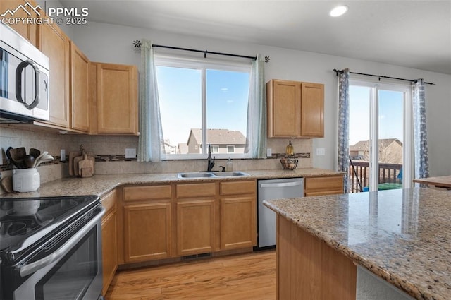 kitchen with stainless steel appliances, tasteful backsplash, a sink, light stone countertops, and light wood-type flooring