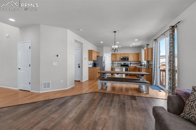 kitchen with visible vents, appliances with stainless steel finishes, open floor plan, a sink, and wood finished floors