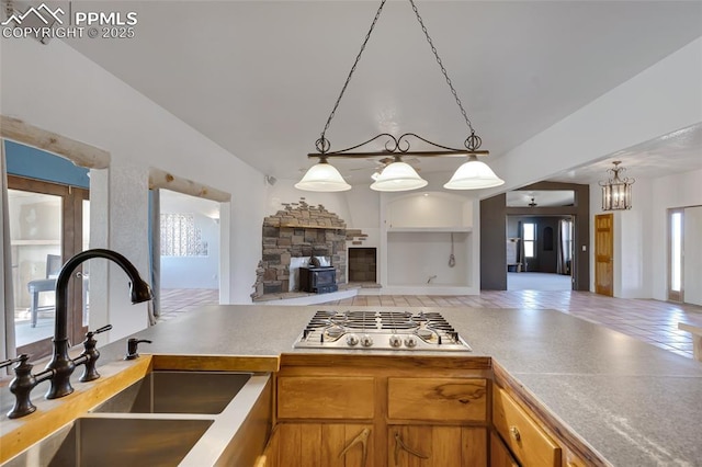 kitchen with brown cabinets, open floor plan, stainless steel gas cooktop, pendant lighting, and a sink