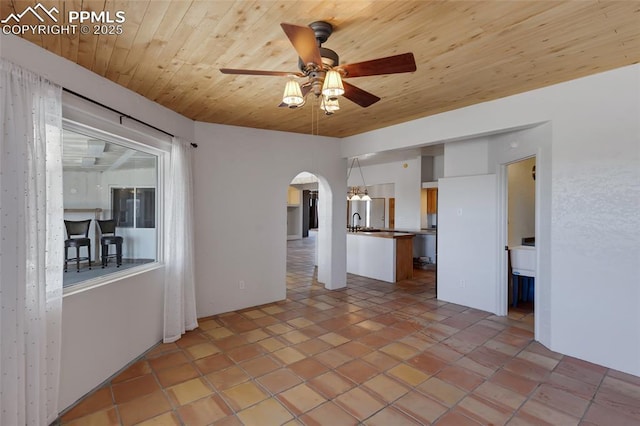 empty room featuring wooden ceiling, ceiling fan, arched walkways, and a sink