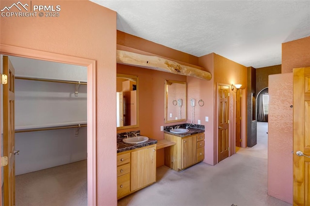 bathroom featuring a textured ceiling, a spacious closet, two vanities, and a sink