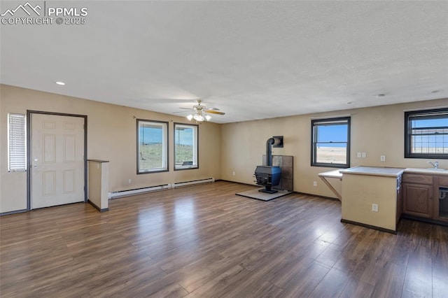 interior space with a ceiling fan, dark wood-style floors, a wood stove, baseboard heating, and a sink