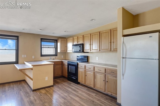 kitchen with light countertops, light wood finished floors, black appliances, and a peninsula