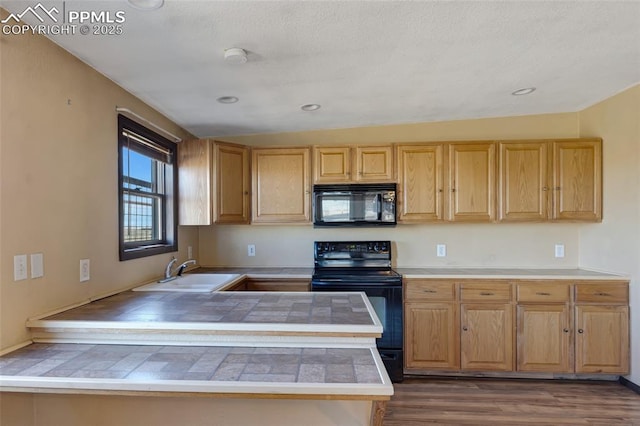 kitchen featuring dark wood-type flooring, a peninsula, vaulted ceiling, black appliances, and a sink