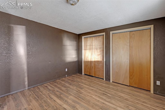 unfurnished bedroom featuring a textured ceiling, baseboards, wood finished floors, and multiple closets