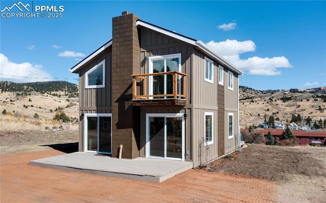 back of house featuring a mountain view, board and batten siding, a chimney, and a balcony