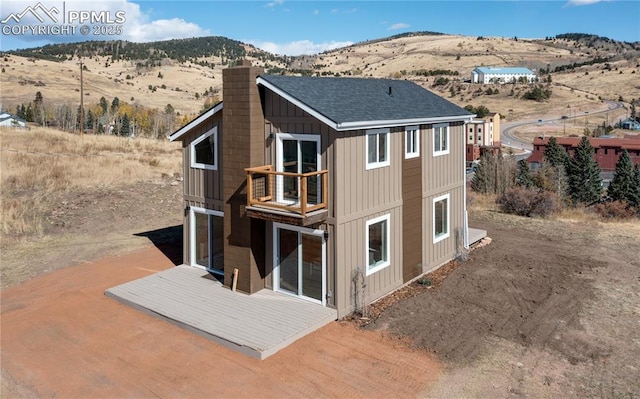 back of property featuring a shingled roof, a chimney, a mountain view, and board and batten siding