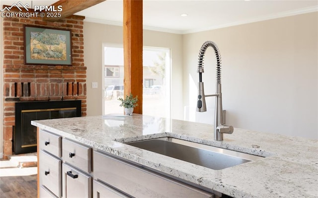 kitchen with crown molding, light stone counters, a sink, and wood finished floors