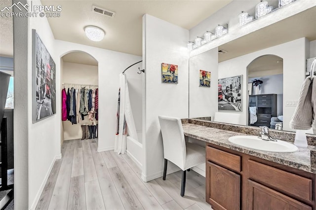 bathroom featuring wood finished floors, vanity, visible vents, baseboards, and shower / bath combo