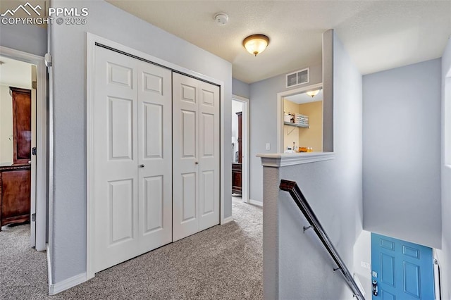 hall featuring carpet floors, visible vents, a textured ceiling, an upstairs landing, and baseboards