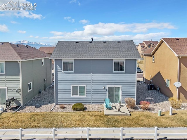 rear view of house with a shingled roof, a mountain view, a yard, and central AC unit