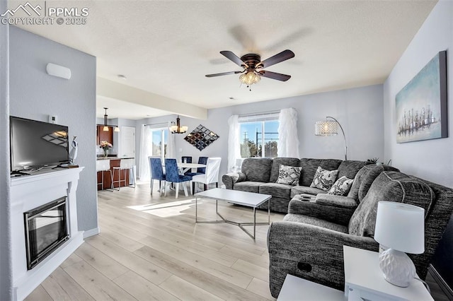 living area with light wood-type flooring, ceiling fan, a textured ceiling, and a glass covered fireplace