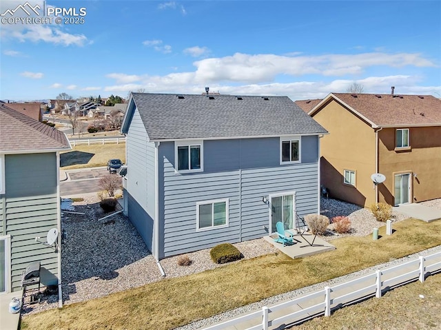 back of property with a yard, roof with shingles, and fence