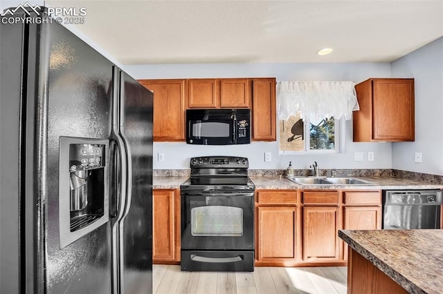 kitchen with brown cabinetry, light wood-style flooring, black appliances, a sink, and recessed lighting