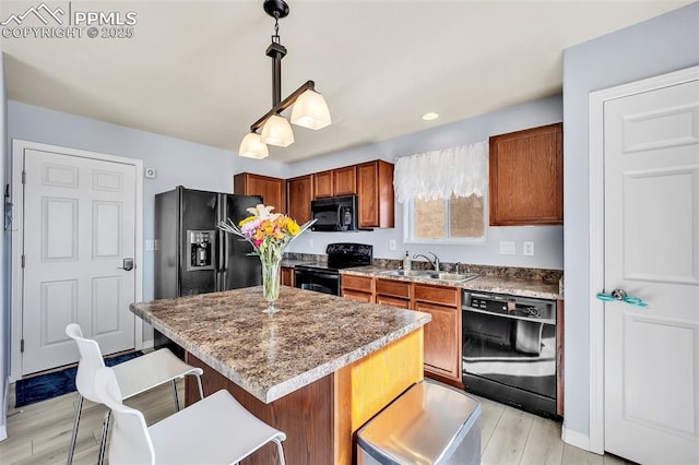 kitchen featuring decorative light fixtures, brown cabinetry, a sink, black appliances, and a kitchen breakfast bar