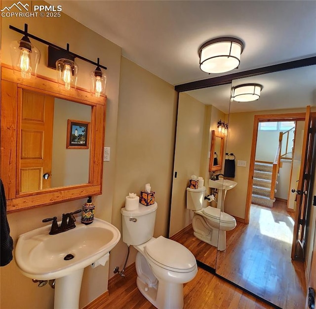 half bath with baseboards, toilet, and wood finished floors