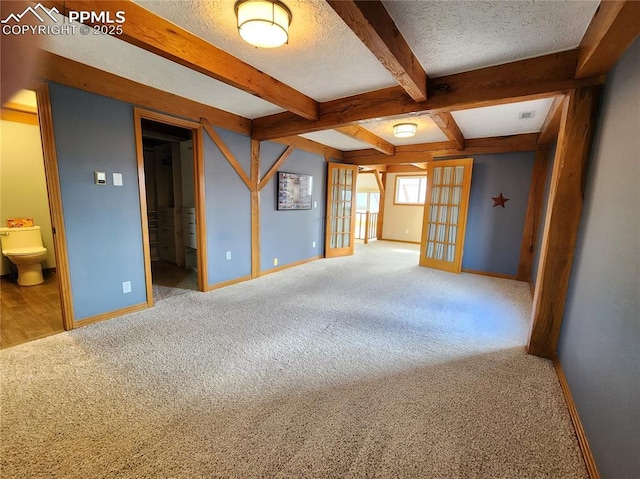 unfurnished room with beam ceiling, a textured ceiling, french doors, carpet flooring, and baseboards