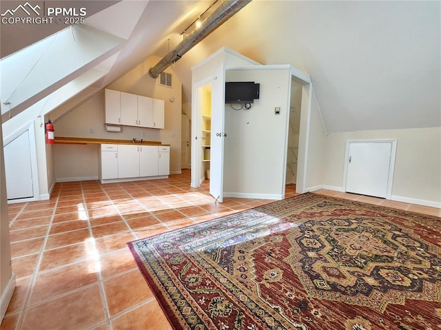 additional living space with light tile patterned floors, visible vents, baseboards, and vaulted ceiling