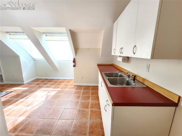 kitchen with light tile patterned floors, baseboards, a skylight, a sink, and white cabinetry