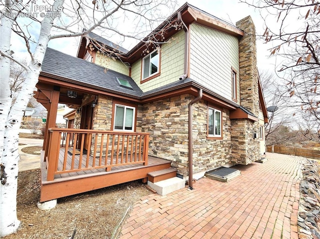 rear view of property featuring a patio, a wooden deck, stone siding, and a chimney