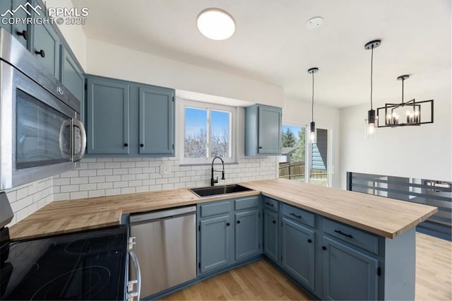 kitchen with wood counters, appliances with stainless steel finishes, a peninsula, blue cabinetry, and a sink