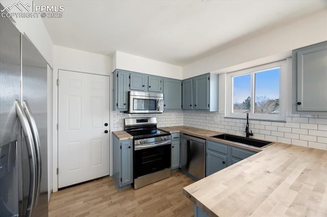 kitchen featuring tasteful backsplash, butcher block counters, appliances with stainless steel finishes, light wood-type flooring, and a sink