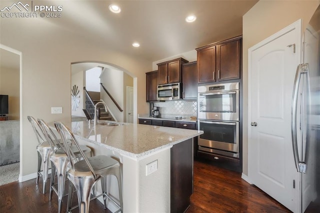 kitchen featuring a sink, light stone counters, tasteful backsplash, appliances with stainless steel finishes, and dark brown cabinets