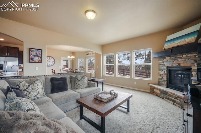 living area featuring baseboards, a fireplace, arched walkways, light carpet, and a chandelier