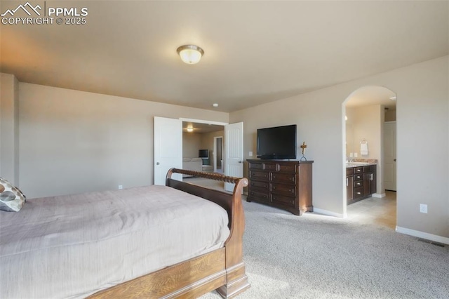 bedroom featuring visible vents, light carpet, ensuite bathroom, arched walkways, and baseboards