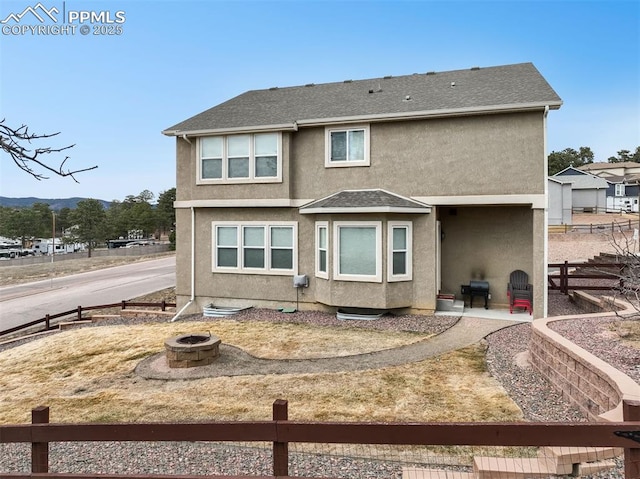 rear view of property featuring stucco siding, a fire pit, a shingled roof, and fence