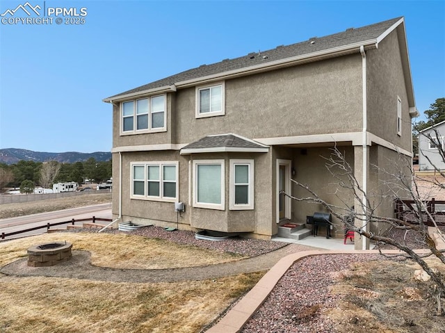 back of property featuring a mountain view, stucco siding, entry steps, and a fire pit