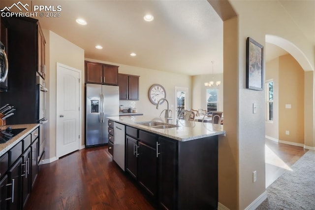 kitchen with light stone countertops, recessed lighting, arched walkways, stainless steel appliances, and a sink