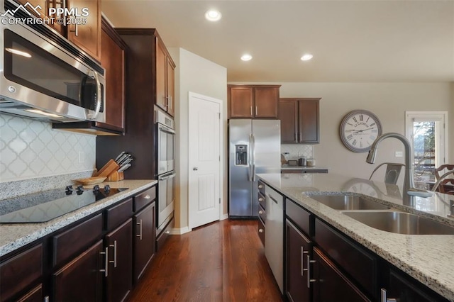 kitchen featuring light stone counters, dark wood finished floors, recessed lighting, a sink, and appliances with stainless steel finishes