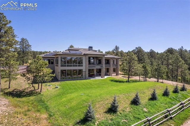 back of property featuring a chimney, solar panels, a lawn, and a patio area