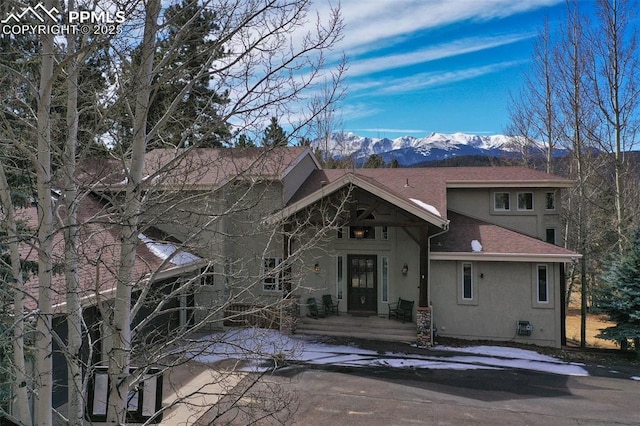 back of property with a mountain view, roof with shingles, and stucco siding