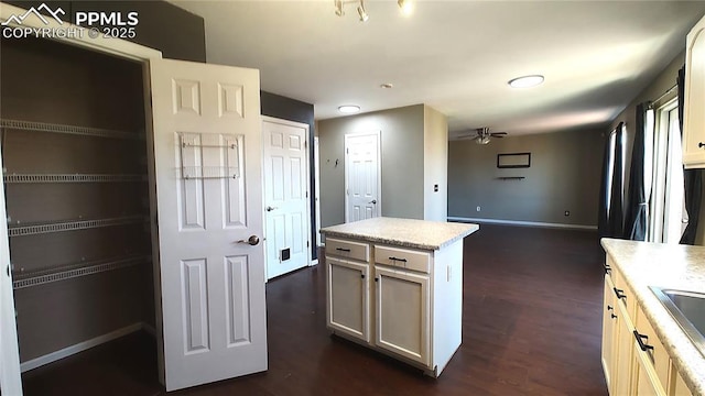 kitchen with dark wood-style floors, a sink, a ceiling fan, and baseboards