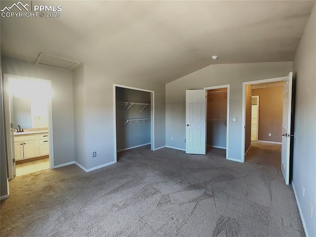 unfurnished bedroom featuring attic access, a sink, carpet, vaulted ceiling, and multiple closets