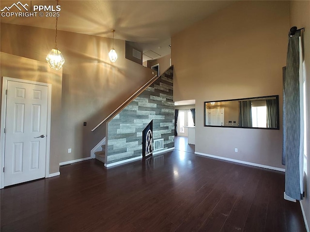 unfurnished living room with baseboards, wood finished floors, stairs, a high ceiling, and a fireplace